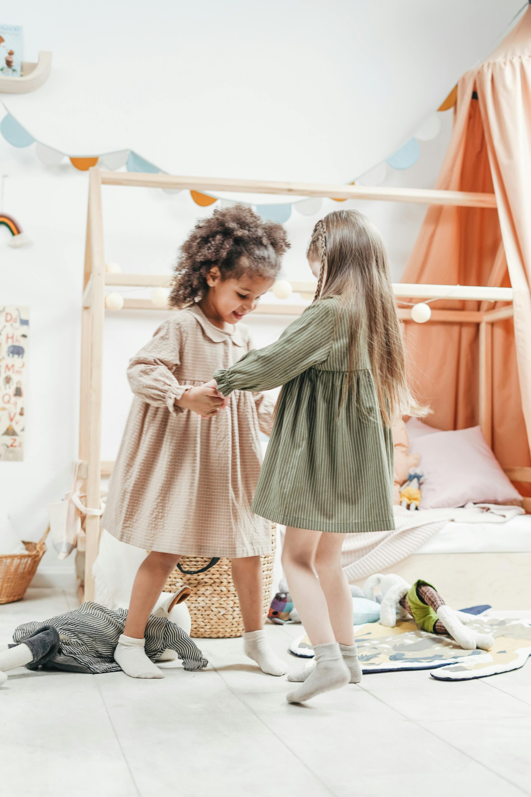 Two young girls enjoy dancing together in a cozy playroom, embodying childhood friendship and joy.